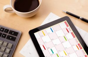 Workplace with tablet pc showing calendar and a cup of coffee on a wooden work table close up - What is Event Marketing? Going Through the Basics